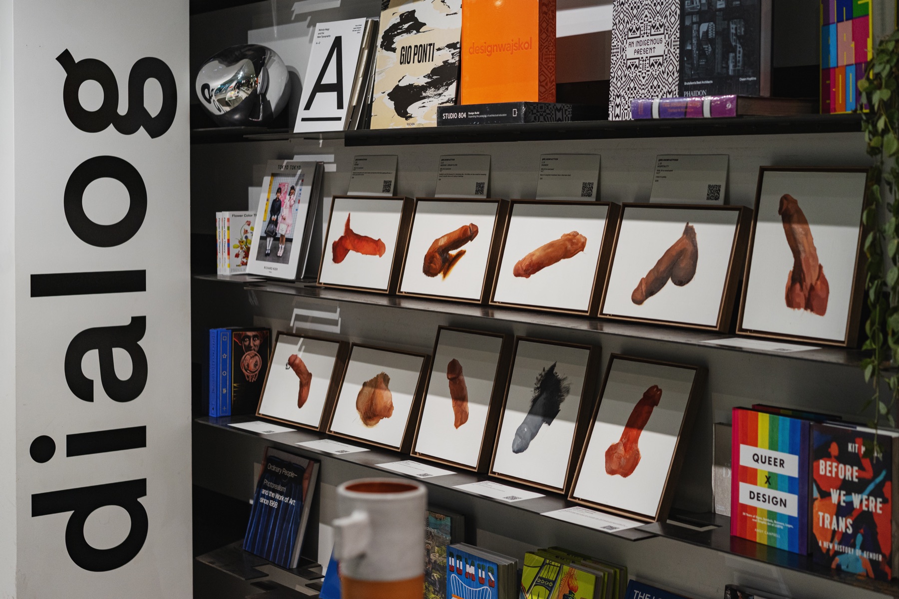 A broad installation view of framed paintings arranged among art and design books at Dialog.