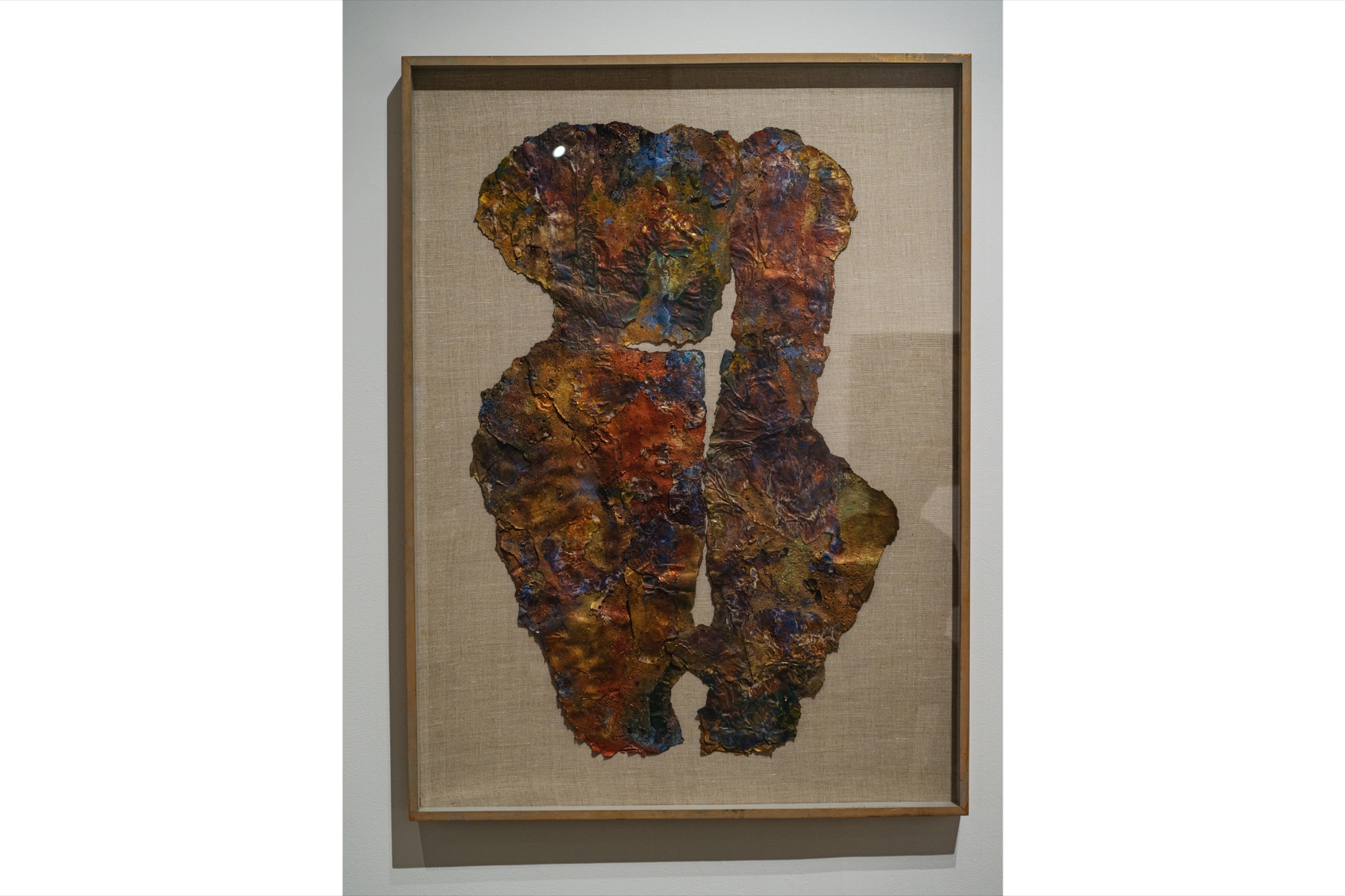 A richly layered rust-colored work is displayed in a wood frame.