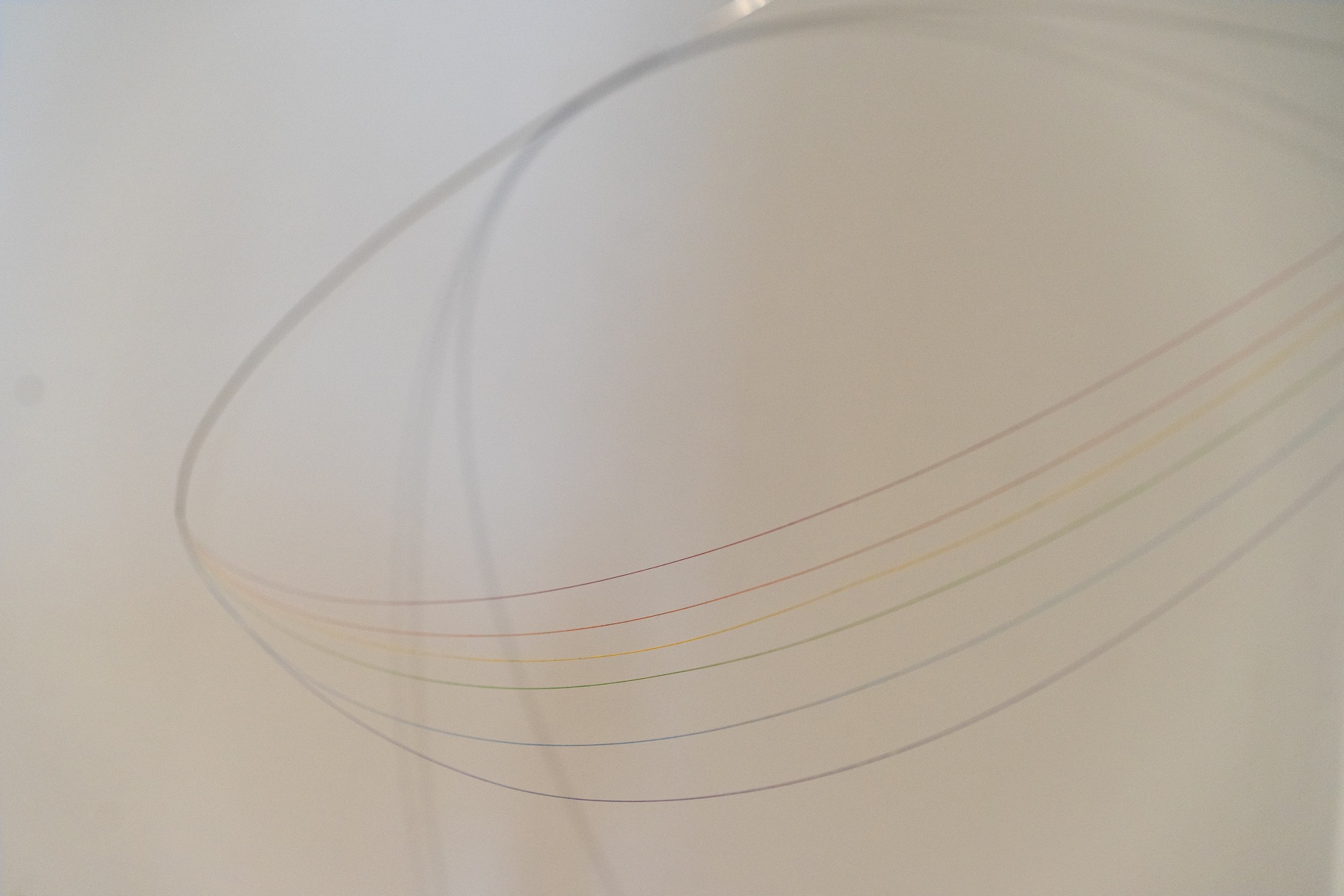 Fine arcs of rainbow-colored light curve across a pale wall.