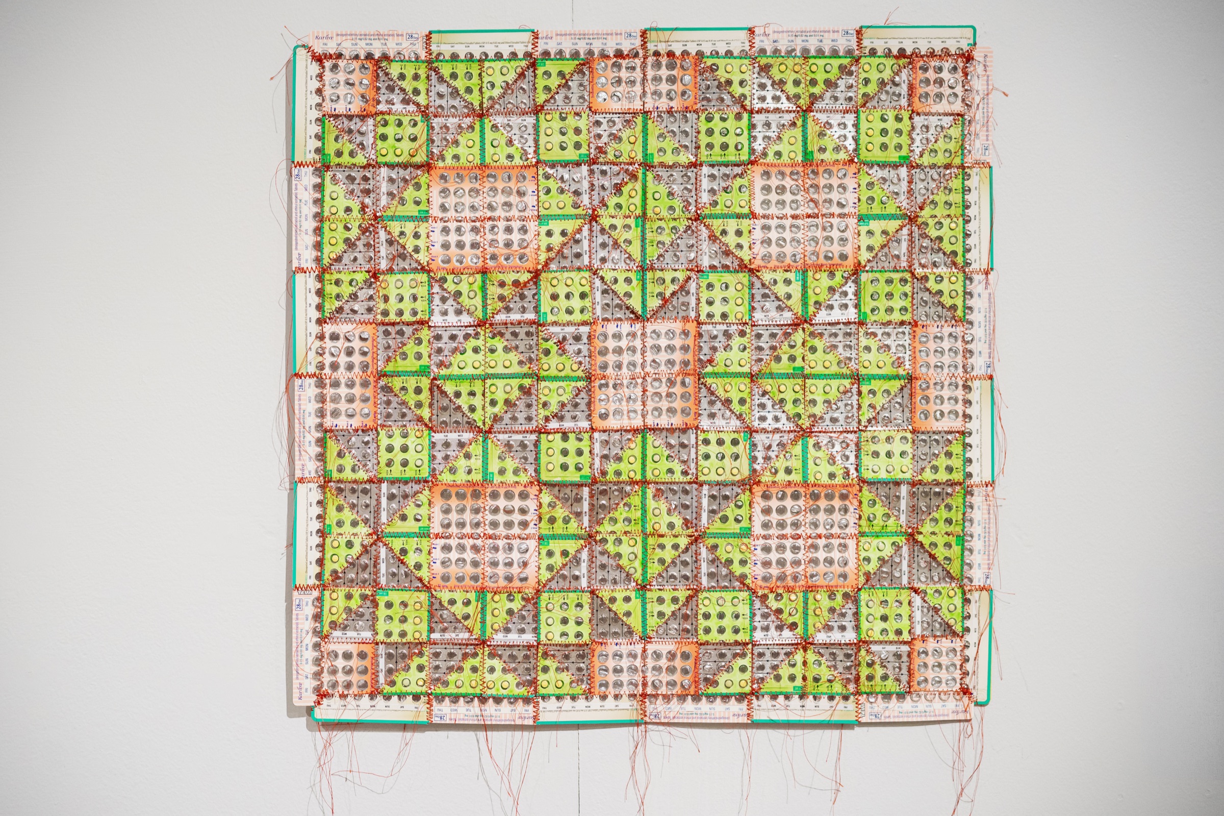 A brightly stitched quilt is assembled from empty medication blister packs.