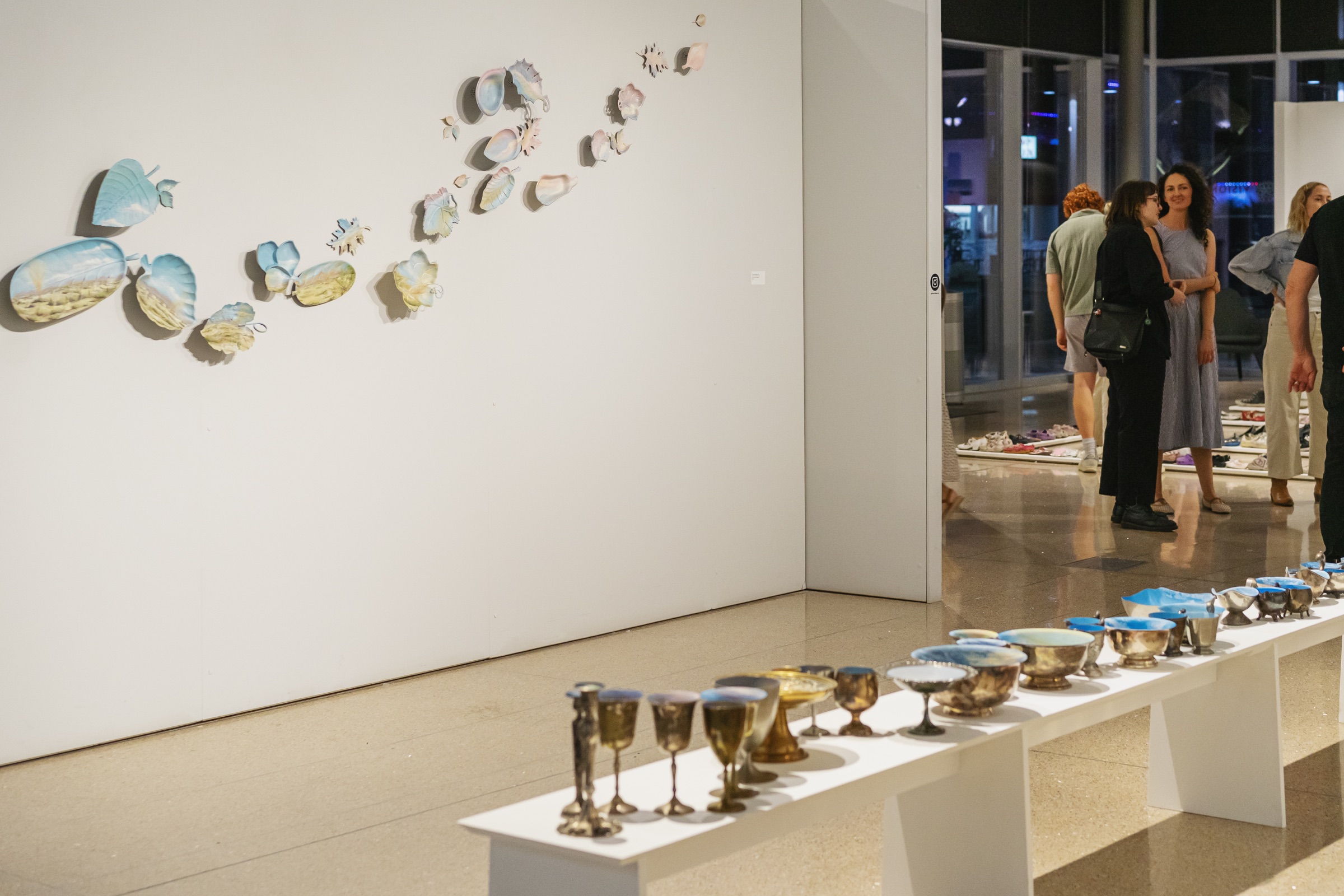 Visitors move through an installation of painted vessels, shoes and wall-mounted objects at Vision Gallery.