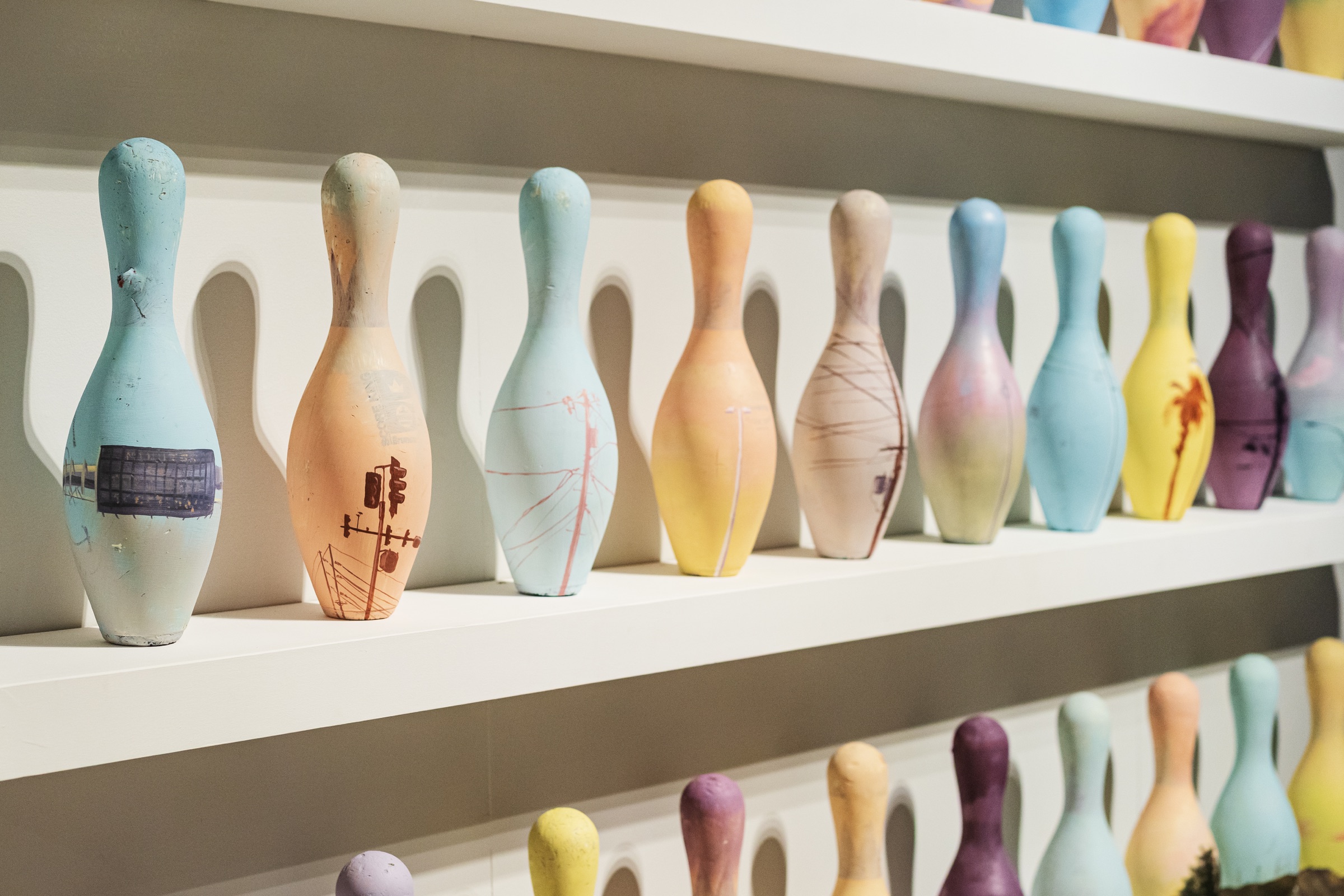 Pastel bowling pins painted with fragments of Phoenix streets line white gallery shelves.