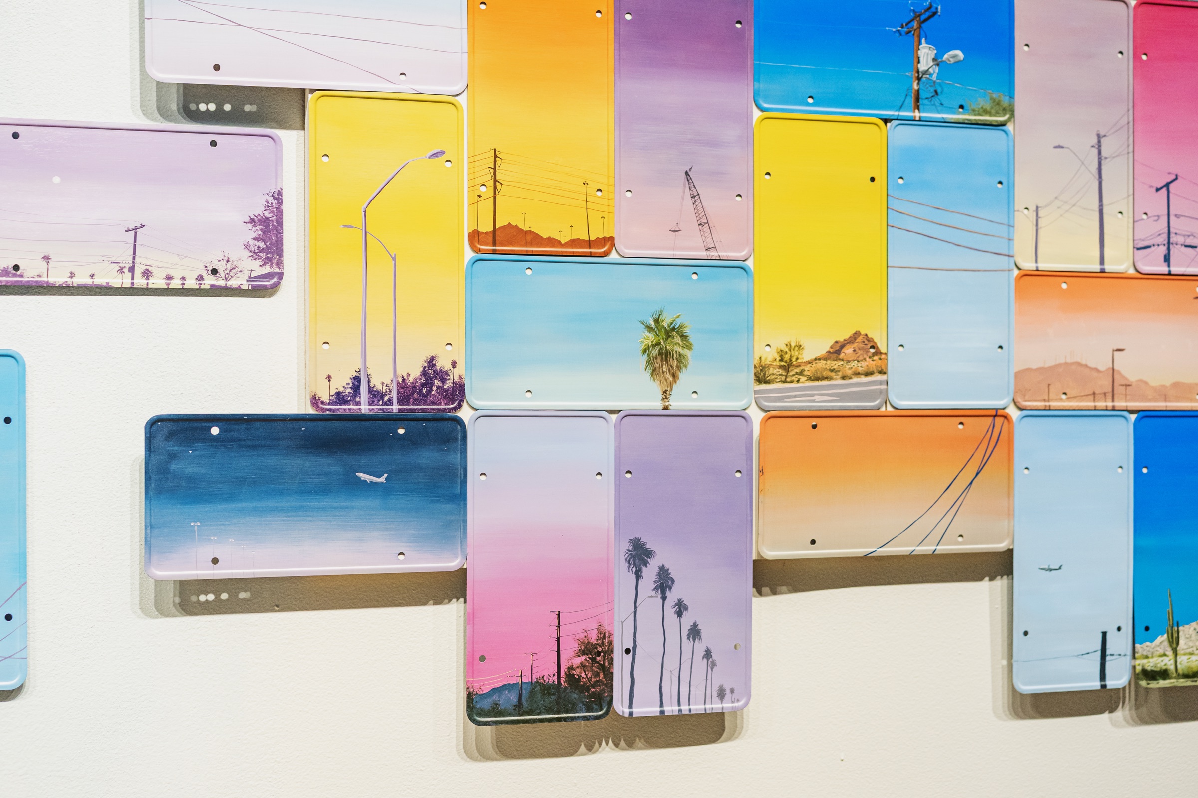 Colorful found plates painted with telephone poles, palms and Phoenix horizons cover a gallery wall.