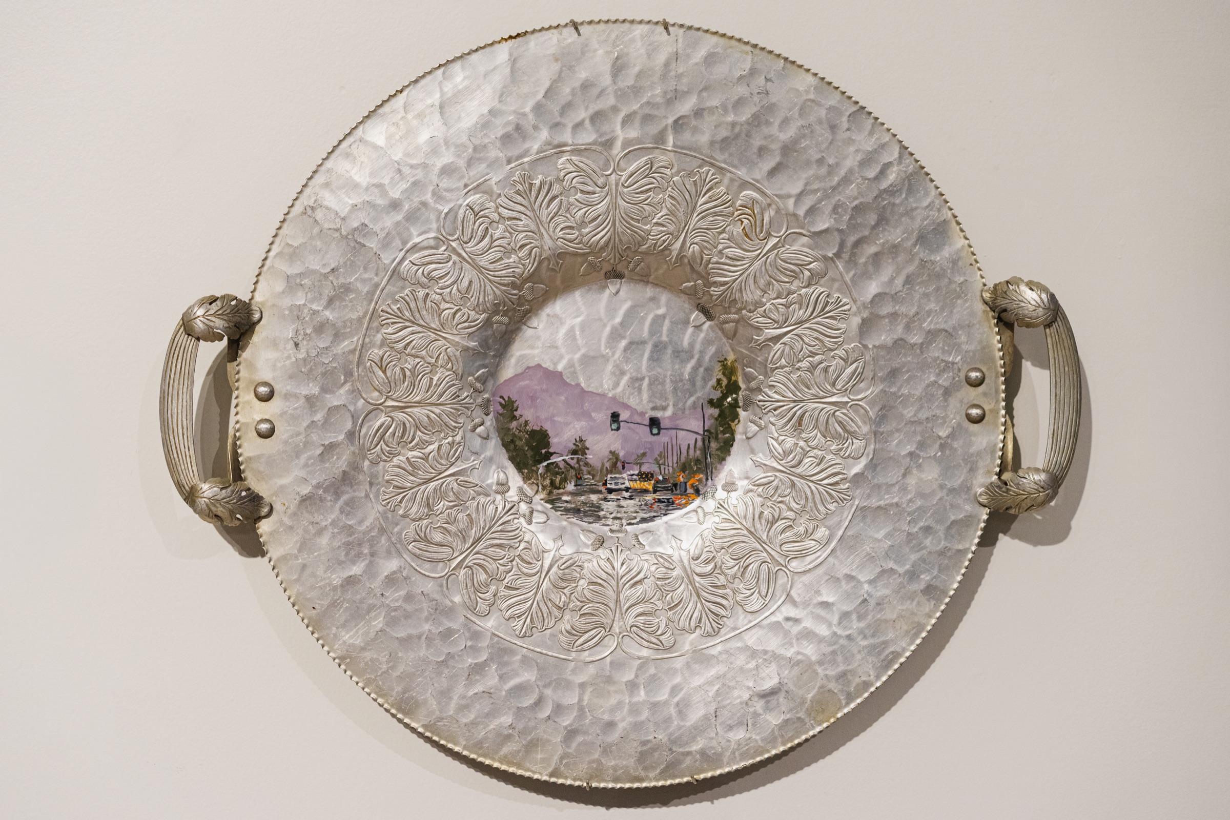 A rainy Phoenix street scene is painted at the center of an ornate silver serving platter.