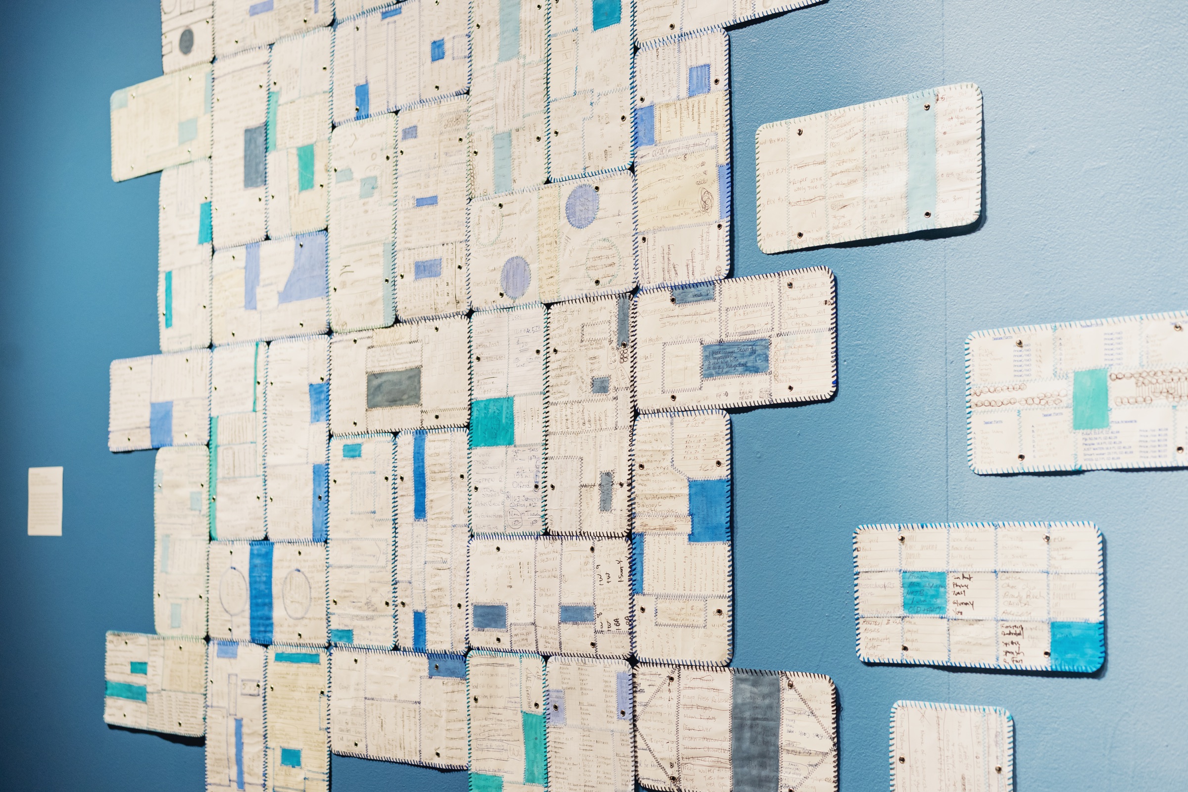 Handwritten medication records are stitched into pale blue and white panels across a blue wall.